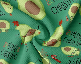 Peut inclure: Tissu vert avec un motif répété de personnages en forme d'avocat portant des lumières de Noël et une étoile rouge. Le texte "Merry Christmas" est répété sur tout le tissu.