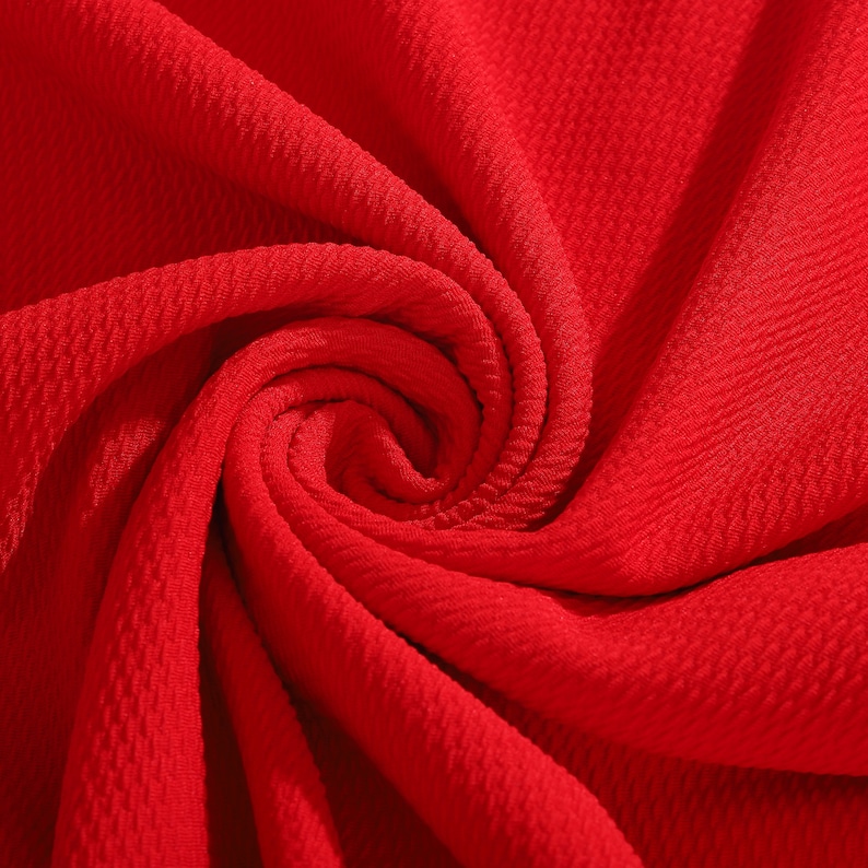 May include: Close-up of a bright red fabric with a textured, woven pattern. The fabric is folded and twisted, creating a swirling effect.