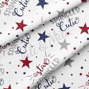May include: White fabric with a repeating pattern of red and gray stars, blue stars, and the text "Spangled Cutie" and "star".