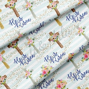 May include: A white fabric with a blue and white striped pattern. The fabric is decorated with a repeating pattern of wooden crosses with floral accents. The crosses have the text "He is Risen" written in blue on them. The fabric is covered in gold glitter.
