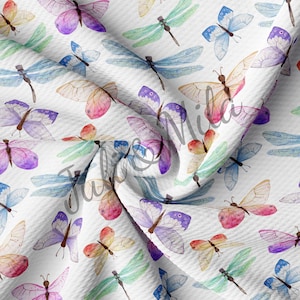 May include: A white fabric with a repeating pattern of colorful butterflies and dragonflies. The butterflies are in shades of pink, purple, blue, and yellow. The dragonflies are in shades of green, blue, and purple.