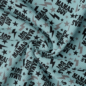 May include: A light blue fabric with a repeating pattern of the words "MAMAS BOY", stars, and lightning bolts in black and gray. The fabric is slightly textured and appears to be folded.