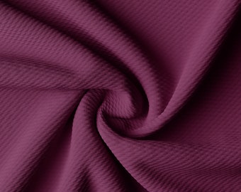 May include: Close-up of a deep burgundy fabric with a textured, waffle-like pattern. The fabric is folded and draped, creating soft, flowing lines.