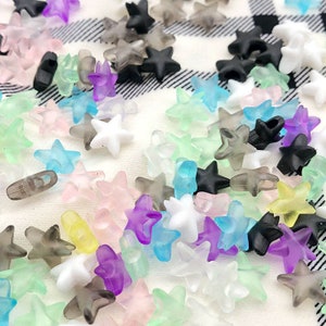 May include: A collection of colorful star-shaped beads in various shades of blue, green, pink, purple, and gray. The beads are made of translucent plastic and have a frosted finish.
