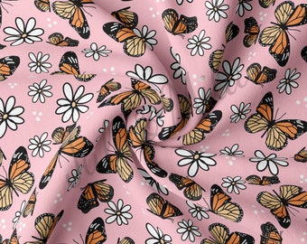May include: A pink fabric with a repeating pattern of orange and black butterflies and white daisies. The fabric is soft and has a subtle sheen.