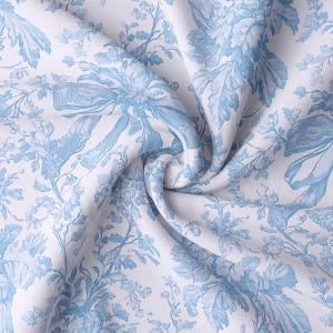May include: White fabric with a blue toile pattern featuring floral and ribbon designs. The fabric is draped, showing the intricate details of the botanical illustrations. The overall aesthetic is classic and elegant.