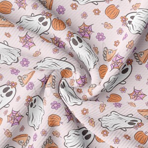 May include: A light pink fabric featuring a repeating pattern of friendly ghosts, pumpkins, spiderwebs, flowers, and autumn leaves. The ghosts wear floral crowns. The pumpkins are orange, and the spiderwebs are pink and orange.