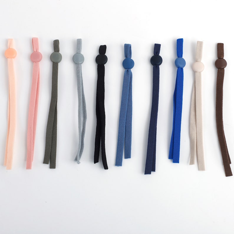 May include: Assortment of 10 colorful elastic straps with adjustable toggles. The straps are made of a soft, stretchy fabric and come in a variety of colors, including pink, green, gray, blue, black, and brown.