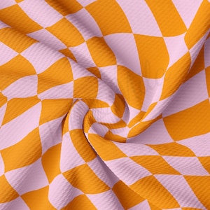 Puede incluir: Una tela con un patrón de cuadros en tonos naranja y rosa. La tela está doblada y tiene textura.