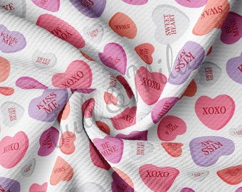 May include: White fabric with a repeating pattern of pink, red, and purple heart-shaped candy with various Valentine's Day messages, such as "Kiss Me", "Sweet Heart", "Be Mine", "I Love You", "XOXO", and "I'm Yours".