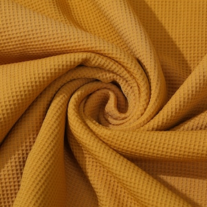 May include: A close-up of a mustard yellow waffle knit fabric. The fabric is soft and textured, with a waffle-like pattern.