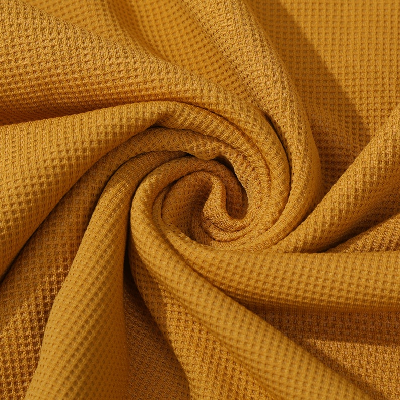 May include: A close-up of a mustard yellow waffle knit fabric. The fabric is soft and textured, with a waffle-like pattern.