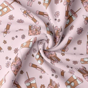 May include: A pink fabric with a repeating pattern of brown pencils, coffee cups, and flowers. The fabric is folded and has a soft, textured look.