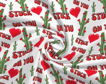 May include: White fabric with a repeating pattern of red hearts, green cacti, and the phrase "Stuck on You" in red letters.