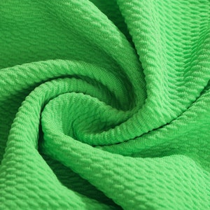 May include: Close-up of a bright green textured fabric. The fabric is folded and twisted, showing the texture and the color.