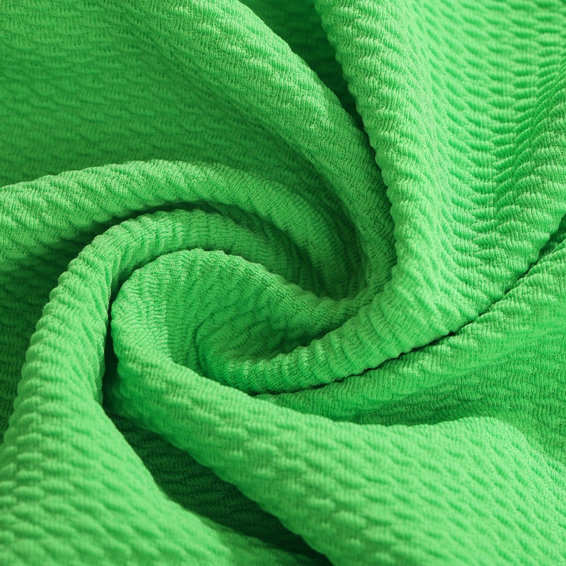 May include: Close-up of a bright green textured fabric. The fabric is folded and twisted, showing the texture and the color.