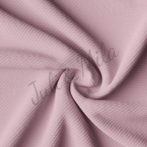 May include: A close-up of a soft, textured fabric in a dusty rose color. The fabric is wrinkled and folded, showing its texture.