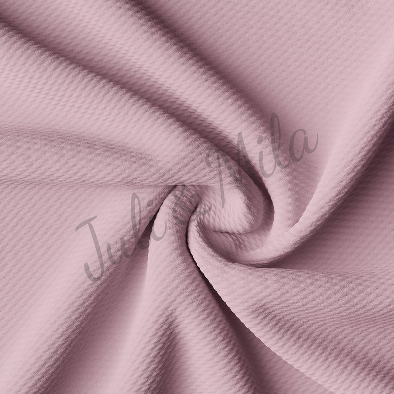May include: A close-up of a soft, textured fabric in a dusty rose color. The fabric is wrinkled and folded, showing its texture.