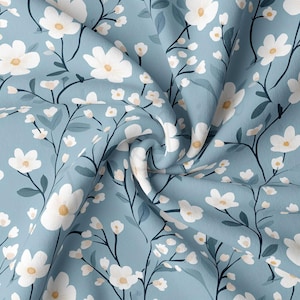 May include: A light blue fabric with a repeating floral pattern. White flowers with yellow centers and dark green stems and leaves are scattered across the fabric. The fabric is slightly wrinkled, creating shadows and depth.