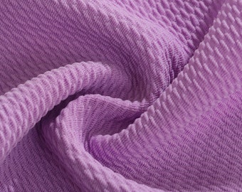 May include: Close-up of a soft, purple fabric with a textured, ribbed pattern. The fabric is folded and draped, showing the texture and drape of the material.