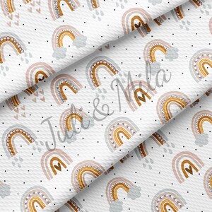May include: White fabric with a repeating pattern of rainbows, hearts, and raindrops. The rainbows feature shades of brown, pink, and blue with black polka dots. The design is suitable for various craft projects.