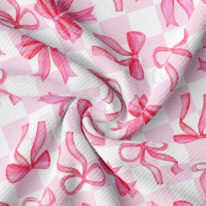 Puede incluir: Tela a cuadros rosa y blanca con un patrón repetido de lazos de satén rosa. Los lazos están dispuestos en un patrón escalonado.