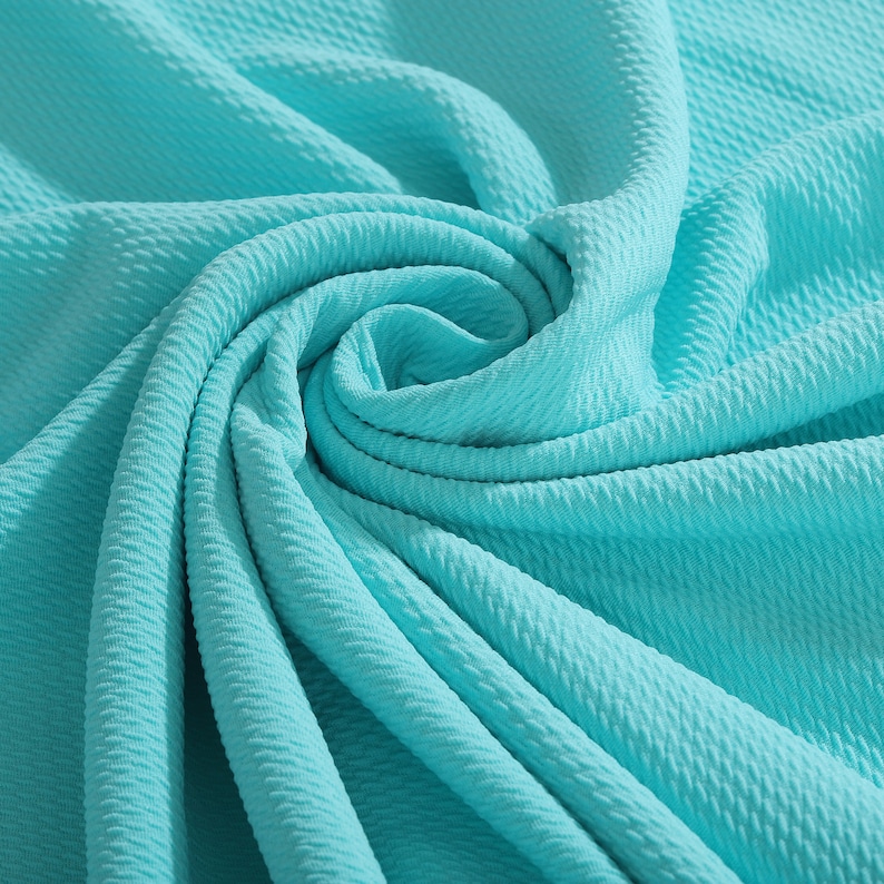 May include: A close-up of a turquoise textured fabric. The fabric is folded and draped, creating a soft and flowing look.
