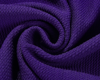 May include: Close-up of a purple textured fabric with a ribbed pattern. The fabric is folded and twisted, showing the texture and depth of the material.