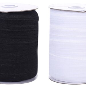 Pode incluir: Dois rolos de elástico, um preto e um branco. O elástico está enrolado em torno de rolos de cartão.