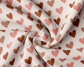 May include: A white fabric with a repeating pattern of brown and pink hearts. The fabric is textured and has a waffle-like appearance.