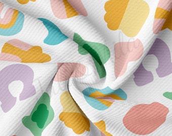 Könnte beinhalten: Ein weißer Stoff mit einem sich wiederholenden Muster aus abstrakten Formen in verschiedenen Farben, darunter Gelb, Rosa, Grün, Blau und Lila.