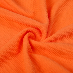 May include: Close-up of a bright orange fabric with a textured, waffle-like pattern. The fabric is folded and draped, showing its soft and flexible texture.