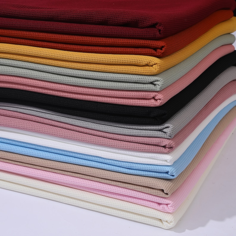 May include: A stack of waffle knit fabric in various colors, including red, orange, yellow, gray, black, pink, white, blue, beige, and ivory.