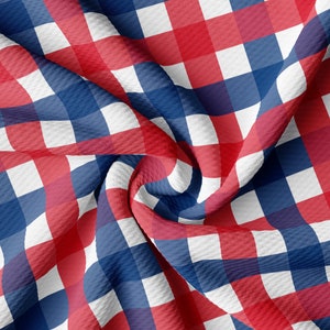May include: A close-up of a fabric with a red, white, and blue checkered pattern. The fabric is textured and has a slight wave pattern. The checks are large and evenly spaced, creating a classic, patriotic design.