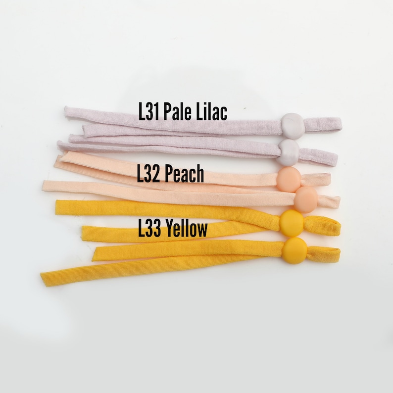 May include: Three strands of elastic cord with plastic toggles. The cords are in three colors: pale lilac, peach, and yellow. The text "L31 Pale Lilac", "L32 Peach", and "L33 Yellow" is printed on the cords.