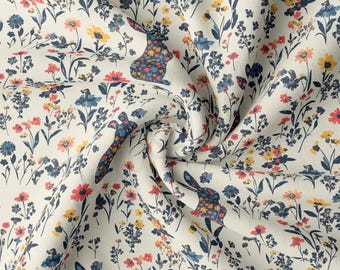 May include: White fabric with a repeating pattern of blue, red, and yellow flowers and stylized bunnies. The fabric is folded and textured.