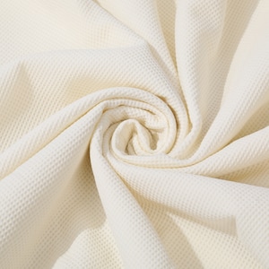 May include: A close-up of a white waffle weave fabric, showing the texture and folds of the material.