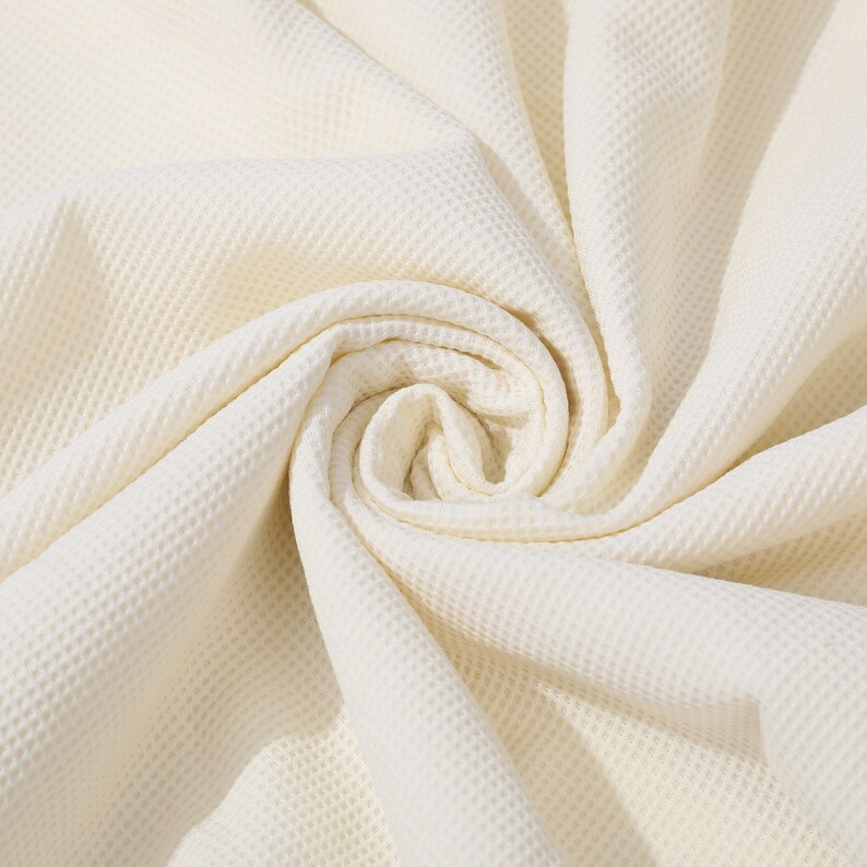 May include: A close-up of a white waffle weave fabric, showing the texture and folds of the material.