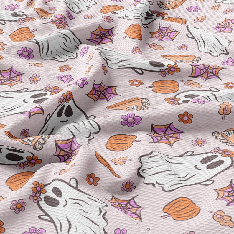 May include: A light pink fabric featuring a repeating pattern of white ghosts with flower crowns, orange pumpkins, purple spiderwebs, and flowers. The fabric has a textured appearance, with a subtle woven design.