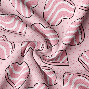 May include: Pink fabric with a repeating pattern of heart-shaped designs. Each heart has a black outline and is filled with pink and white stripes. Small pink speckles are scattered across the background.