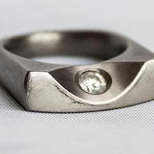 Peut inclure: Une bague en argent avec une bande de forme carrée et un seul diamant clair serti au centre.