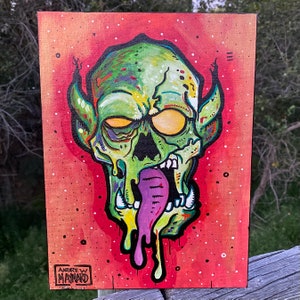 May include: A green and purple monster with a dripping tongue, painted on a red background with white speckles. The monster has a large, open mouth and a pair of pointed ears. The painting is signed "Andrew Maynard" in the bottom left corner.