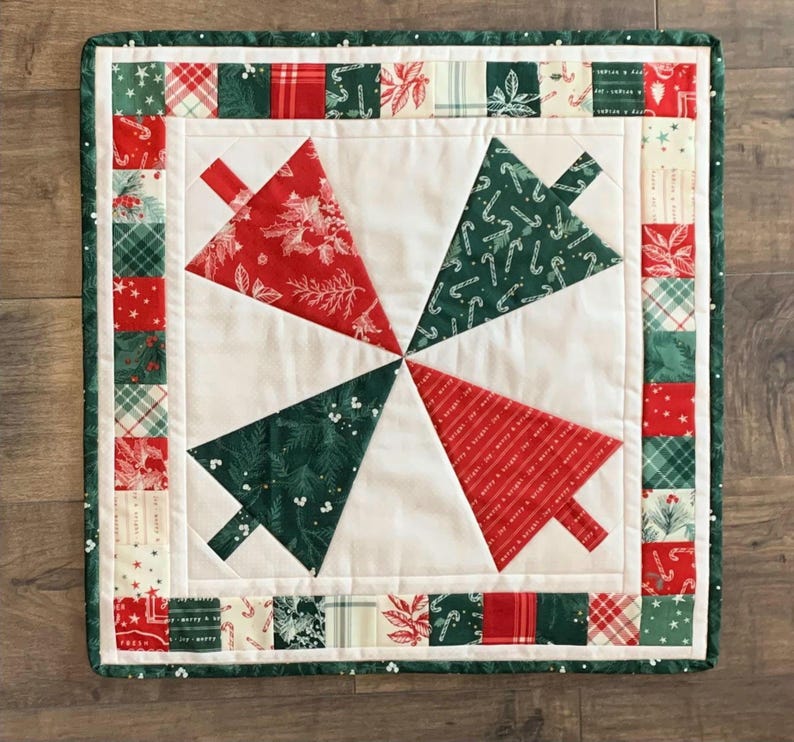 K&ouml;nnte beinhalten: Ein wei&szlig;er gesteppter Tischl&auml;ufer mit einem gr&uuml;nen und roten Weihnachtsbaumdesign. Der L&auml;ufer hat einen Rand aus gr&uuml;nen, roten und wei&szlig;en Stoffquadraten.