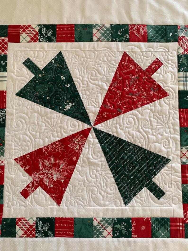 K&ouml;nnte beinhalten: Ein wei&szlig;er gesteppter Stoff mit einem roten und gr&uuml;nen Patchwork-Rand. Die Mitte des Stoffes zeigt vier rote und gr&uuml;ne Weihnachtsbaumformen, jede mit einem anderen Muster.