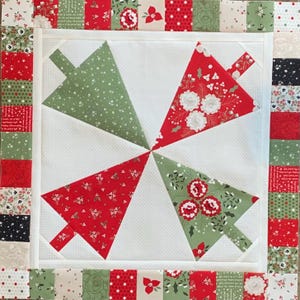 K&ouml;nnte beinhalten: Ein wei&szlig;er Hintergrund mit einem roten und gr&uuml;nen Patchwork-Rand. Die Mitte des Quilts zeigt vier gr&uuml;ne und rote Weihnachtsbaumformen.