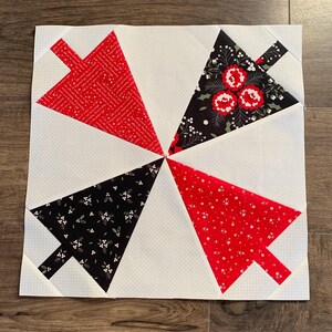 K&ouml;nnte beinhalten: Ein wei&szlig;er Stoffquadrat mit vier roten und schwarzen dreieckigen Stoff-Patches, die darauf gen&auml;ht sind. Jeder Patch hat ein anderes Muster. Die Patches sind in einem Windm&uuml;hlenmuster angeordnet.