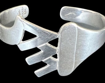 May include: Silver bracelet with a geometric design. The bracelet is open and has a textured finish.