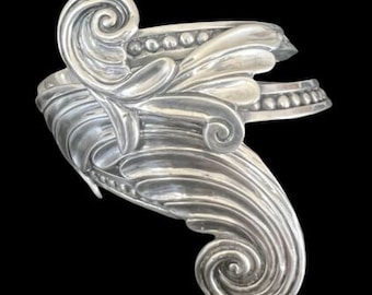 May include: A silver bracelet with a detailed, ornate design featuring swirling, floral patterns.