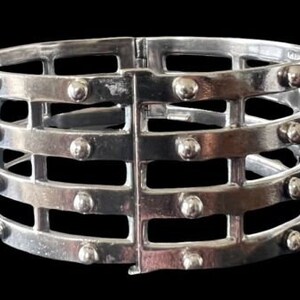 May include: A silver metal bracelet with a cage-like design and studded accents.
