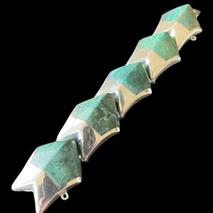 May include: A silver bracelet with green gemstone accents. The bracelet is made of a series of connected star-shaped pieces.
